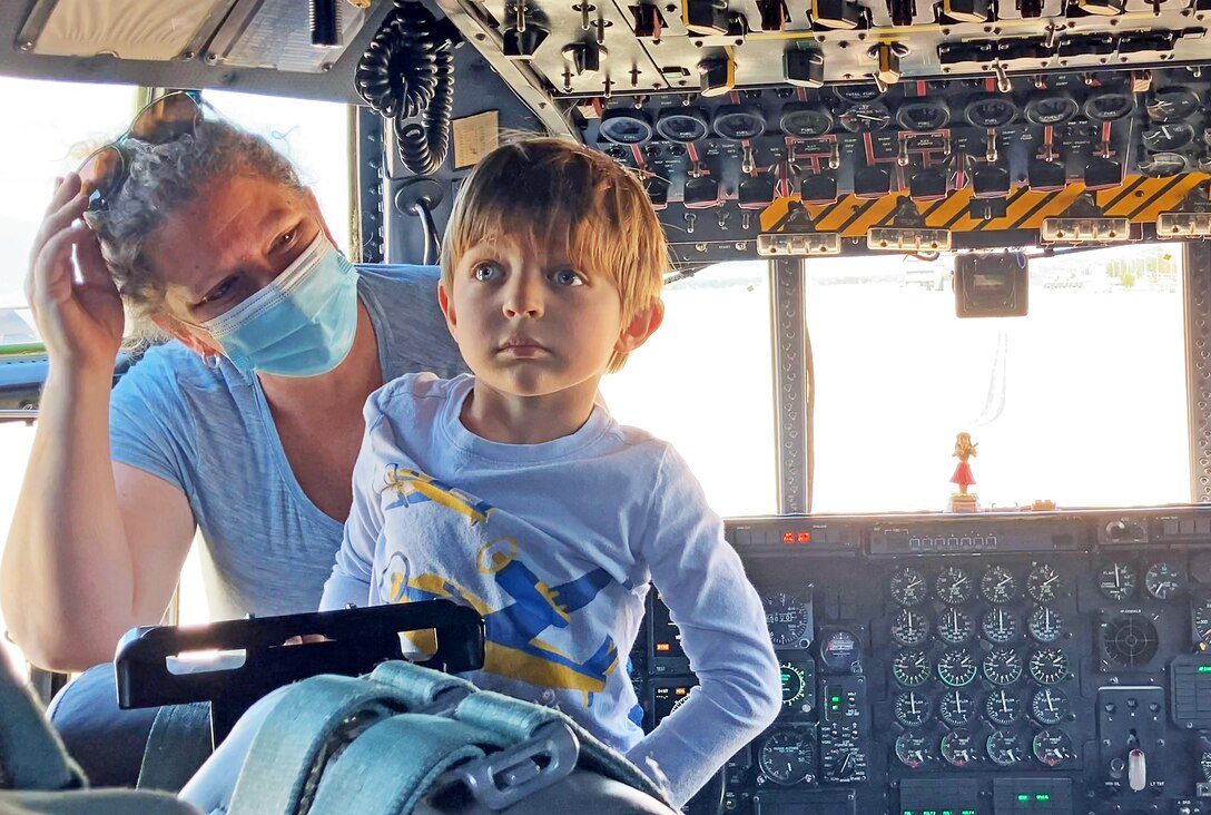 Young boy and mother stand inside cockpit of large plane.