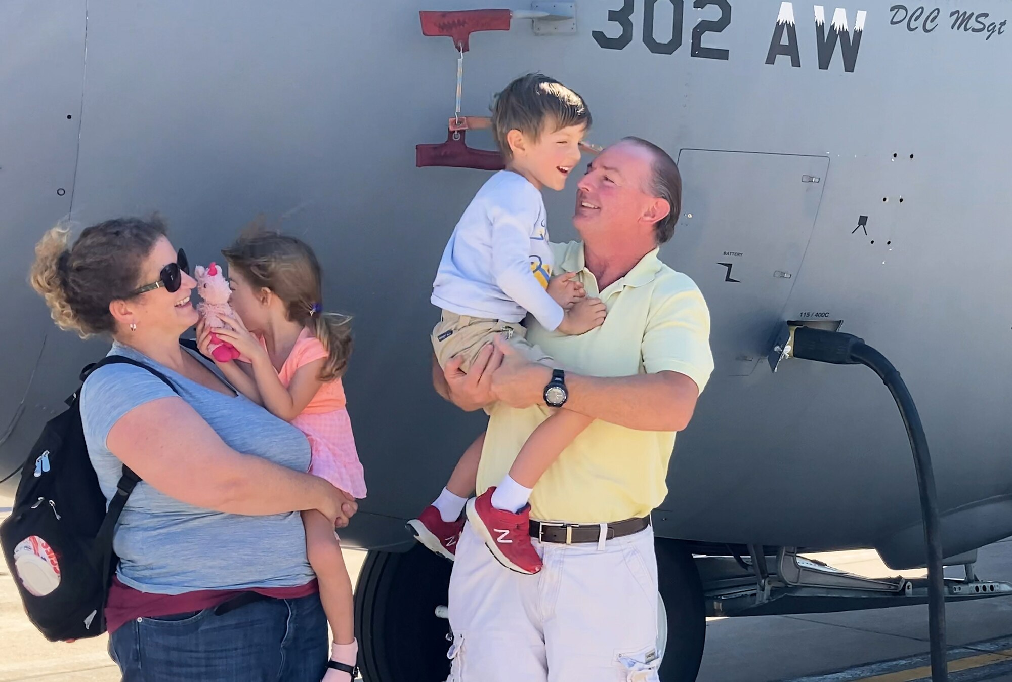 Young boy and family stand in front of large military aircraft on flightline.