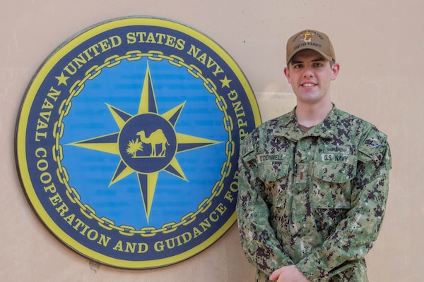 200625-N-IO414-1038 NAVAL SUPPORT ACTIVITY BAHRAIN (June 25, 2020) Ensign Conor O’Donnell poses for a photo in front of U.S. Naval Forces Central Command’s Naval Cooperation and Guidance for Shipping (NCAGS) headquarters. NCAGS serves as a communication link between merchant and military vessels and is made up entirely of U.S. Navy reservists, many of whom are professional merchant marines who leverage their civilian expertise and experience when they report for duty.