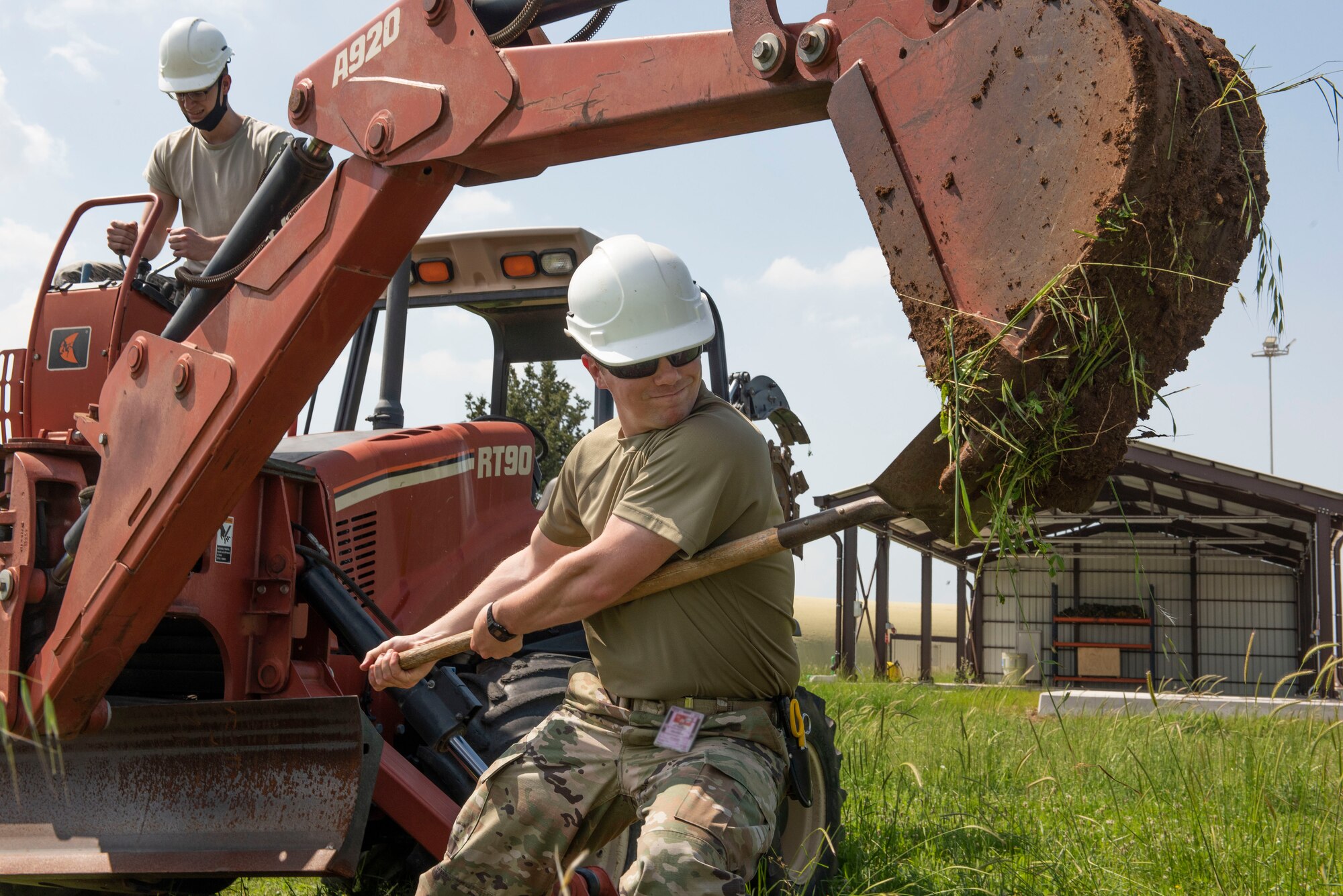 Photo of an Airman using a shovel to dislodge dirt from a trench machine