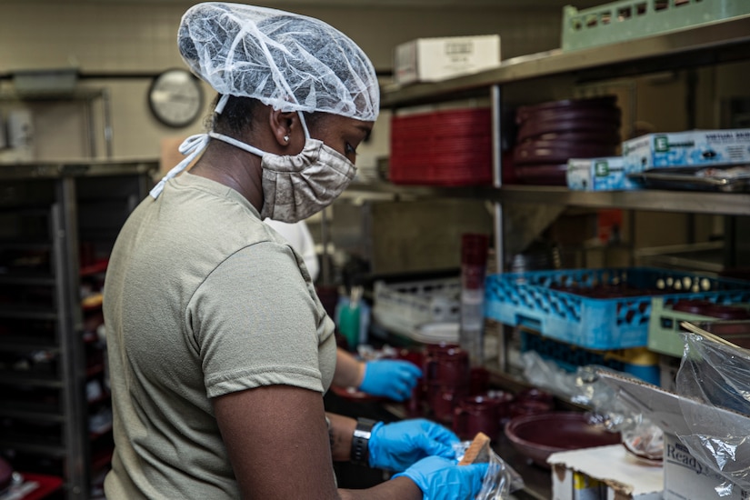 An airman wearing a hairnet, face mask and gloves prepares food.