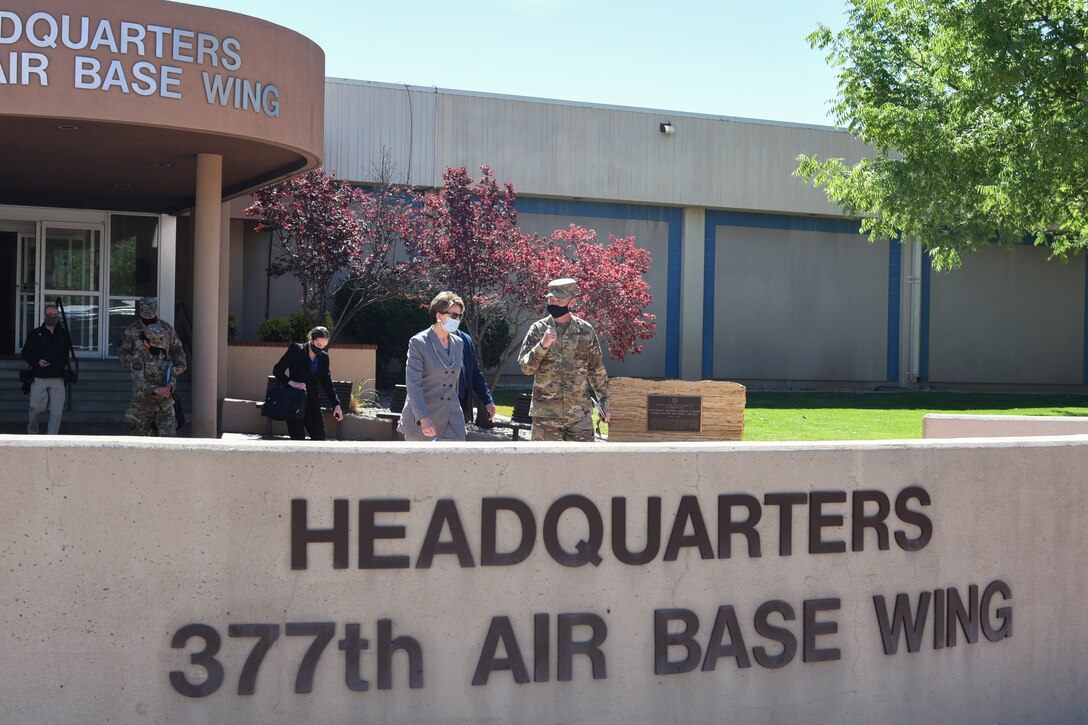 A woman and an airman, both wearing masks, talk while walking out of a headquarters building..