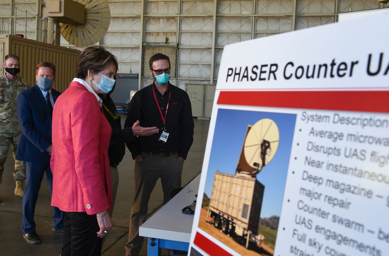 One of three airmen gestures while speaking with a civilian woman outdoors. All are wearing masks.