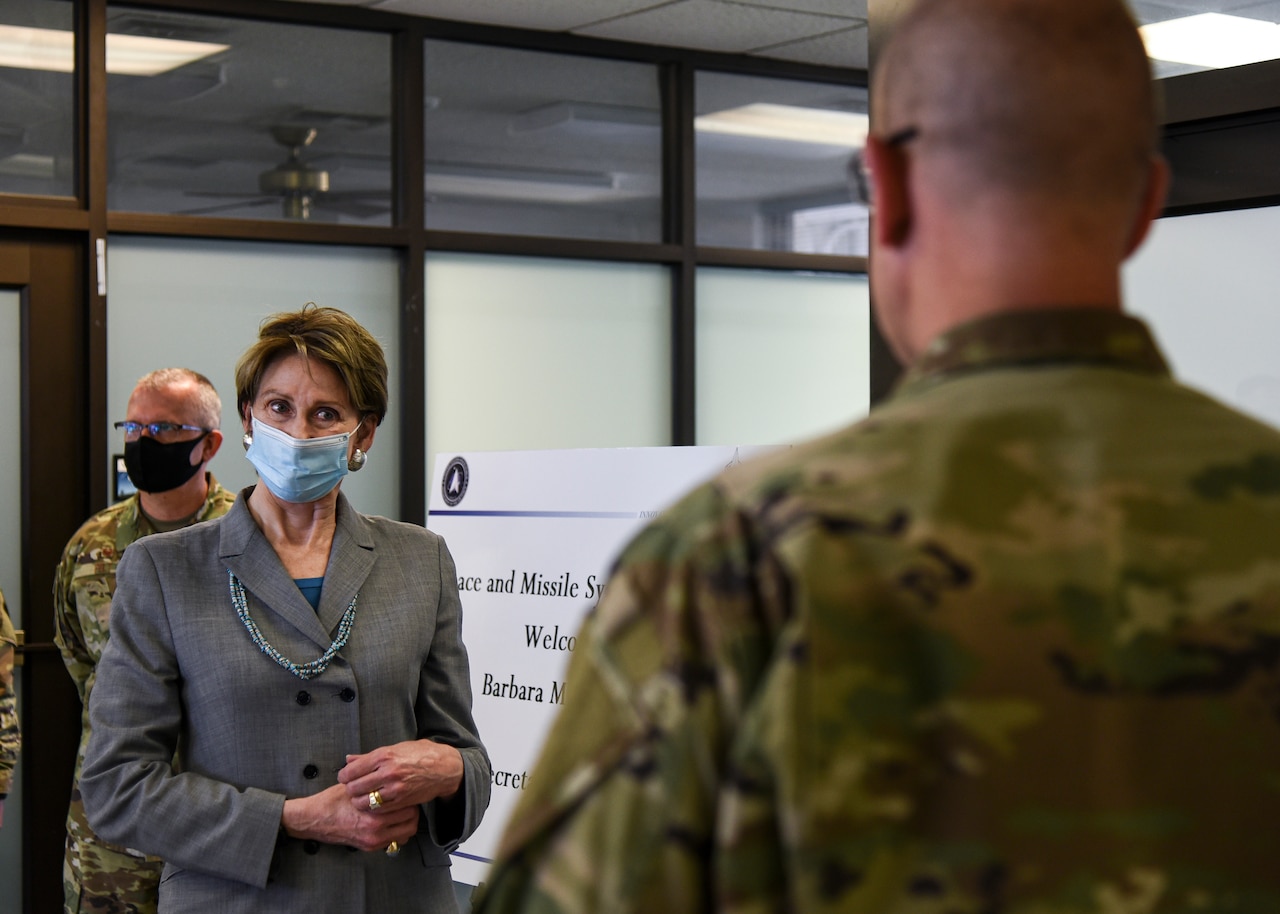 A woman wearing a mask receives a briefing from an airman who has his back to the camera.