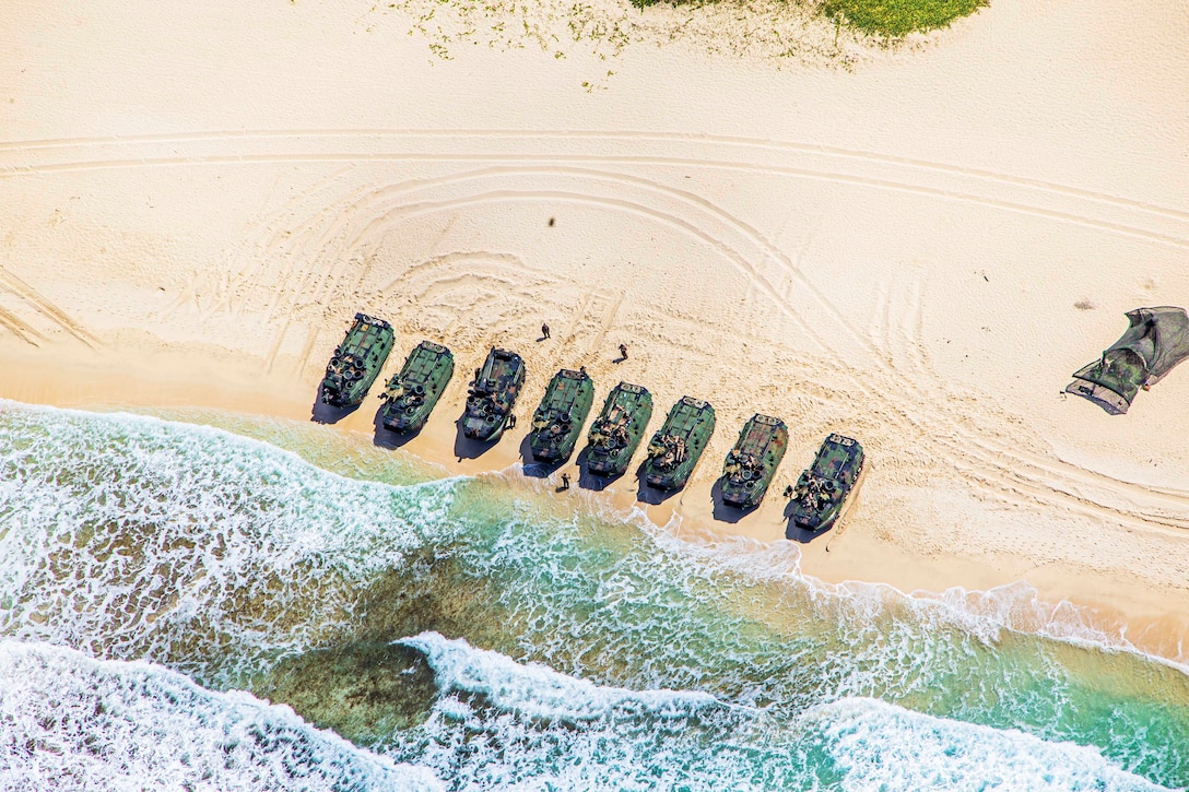 A row of eight vehicles on a beach are seen from above.