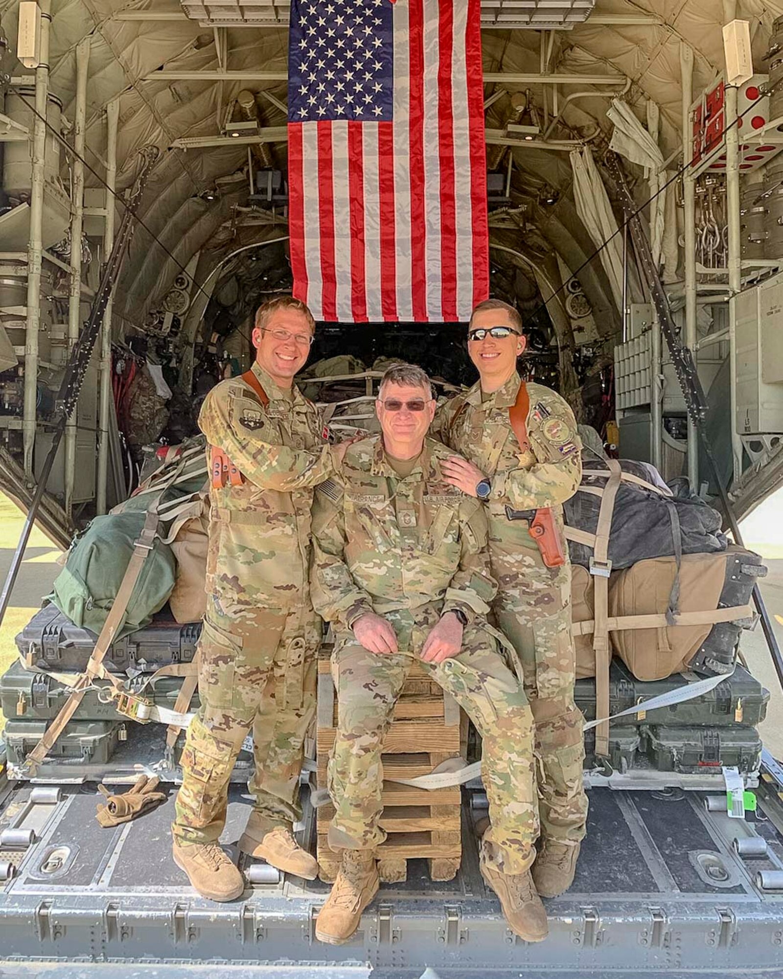 Air Force Reserve Master Sgt. Scott Klobucher (left) and Staff Sgt. Christopher James (right) poses with Chief Master Sgt. Donald Tarrance on the back of a C-130J Hercules loaded with cargo while deployed to Syria in 2019. Tarrance has served for over 40 years in a variety of positions and statuses. (Courtesy photo)