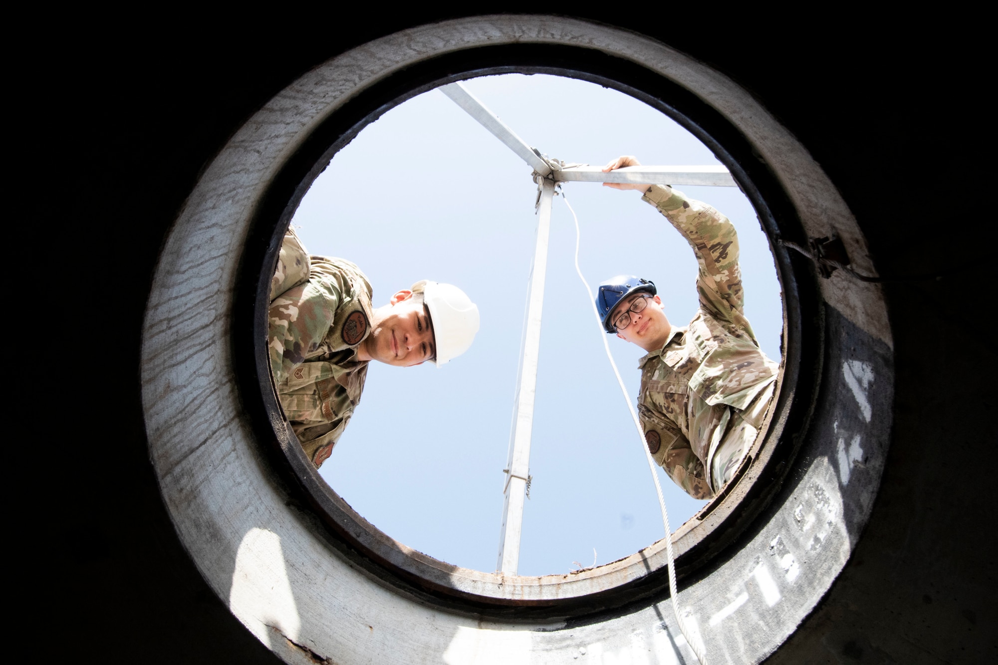 U.S. Air Force Staff Sgt. Alan Hooper, 39th Communications Squadron cable maintenance supervisor, (left), and Senior Airman Jacob Glass, 39th CS cable and antenna systems technician, stare down a manhole May 20, 2020, at Incirlik Air Base, Turkey.  Cable and antenna systems Airmen, popularly called “cable dawgs,” maintain and install cables on telecommunications towers and underground vaults or maintenance holes. (U.S. Air Force photo by Staff Sgt. Joshua Magbanua)