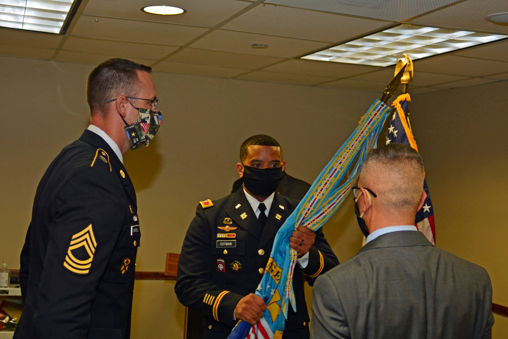 two Army members and a senior civilian member pass a flag in a cermony