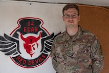Airman stands next to image of 34th ECAB unit seal on the wall behind him