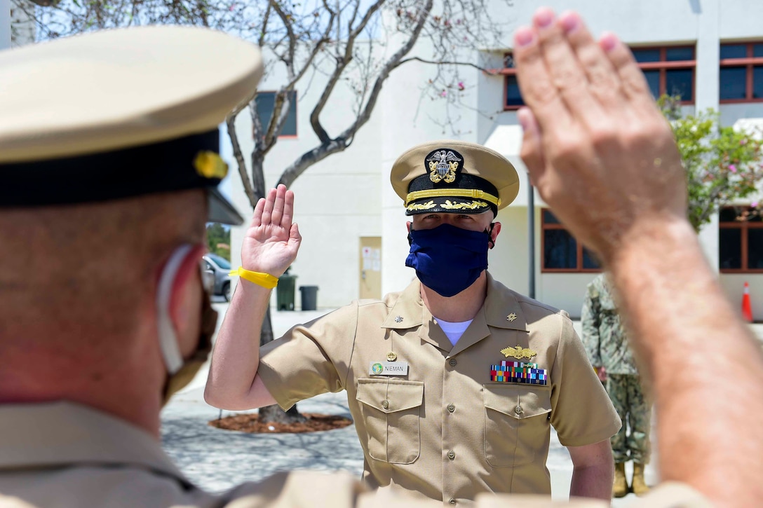 Two sailors face each other and raise their right hands.