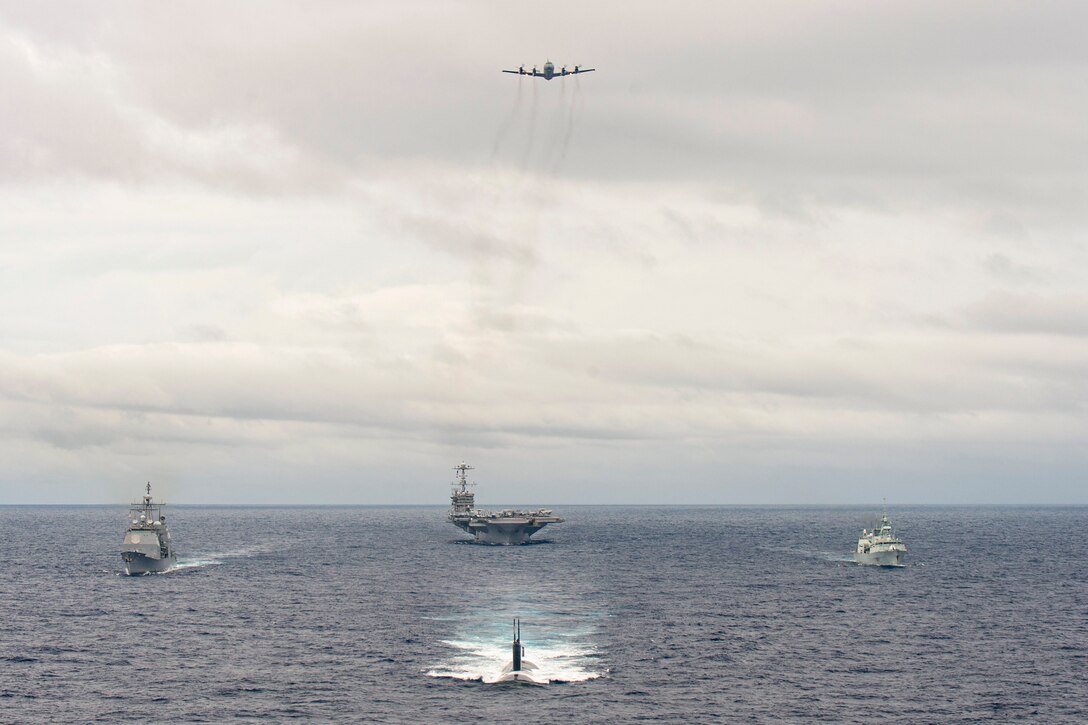 U.S. and Canadian naval ship transits the ocean as a Canadian Air Force aircraft flies above.