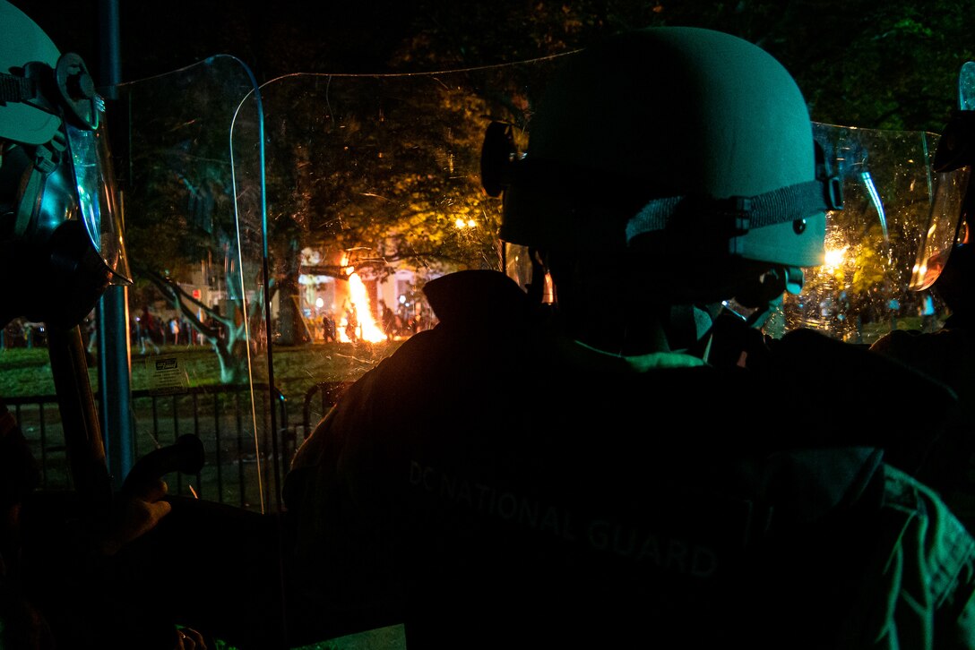 Soldiers watch a fire burn at night.