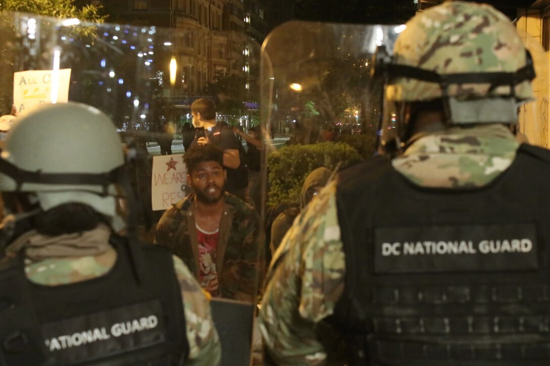 Soldiers face a crowd at night.