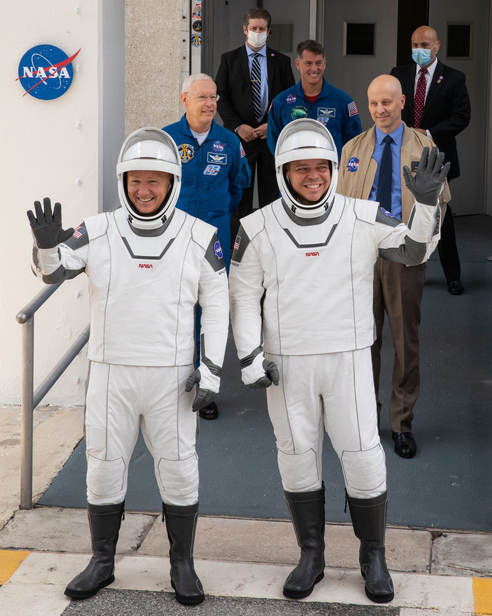 NASA astronauts Douglas Hurley (left) and Robert Behnken wave as they exit the Neil A. Armstrong Operations and Checkout Building at the agency’s Kennedy Space Center in Florida. They were preparing for transport to Launch Complex 39A to launch on NASA’s SpaceX Demo-2 mission.