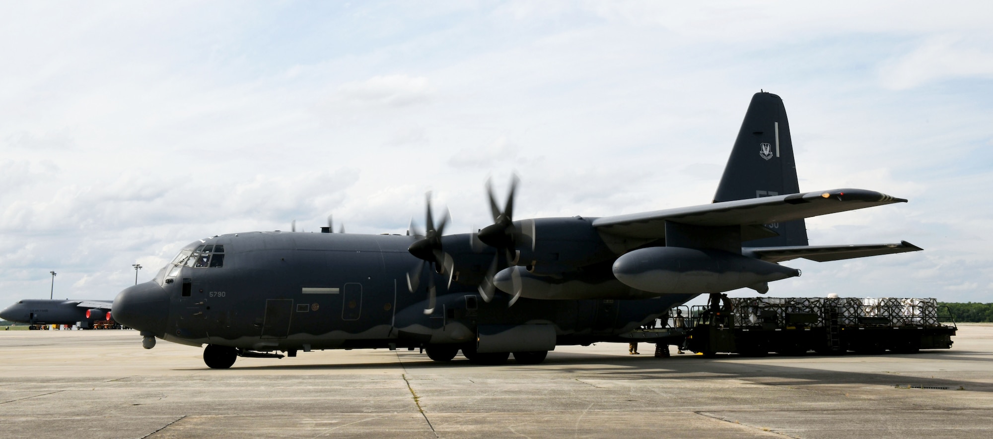 Photo shows C-130 aircraft with truck behind the cargo end of the plane containing pallets with buckets.