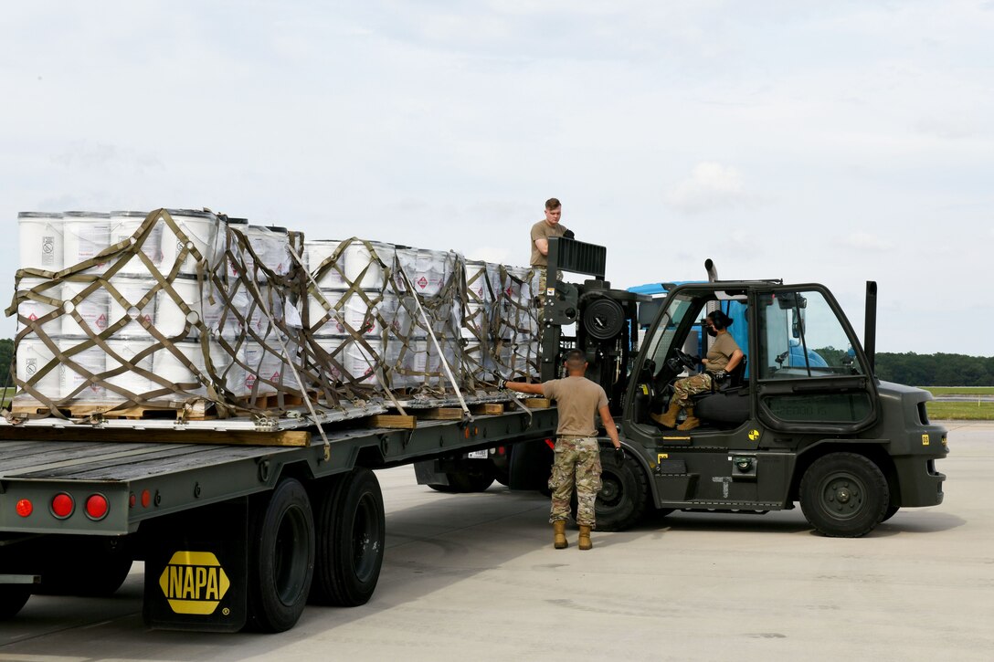 Photo shows three Airmen working on a small flat bed truck loading five pallets of buckets.