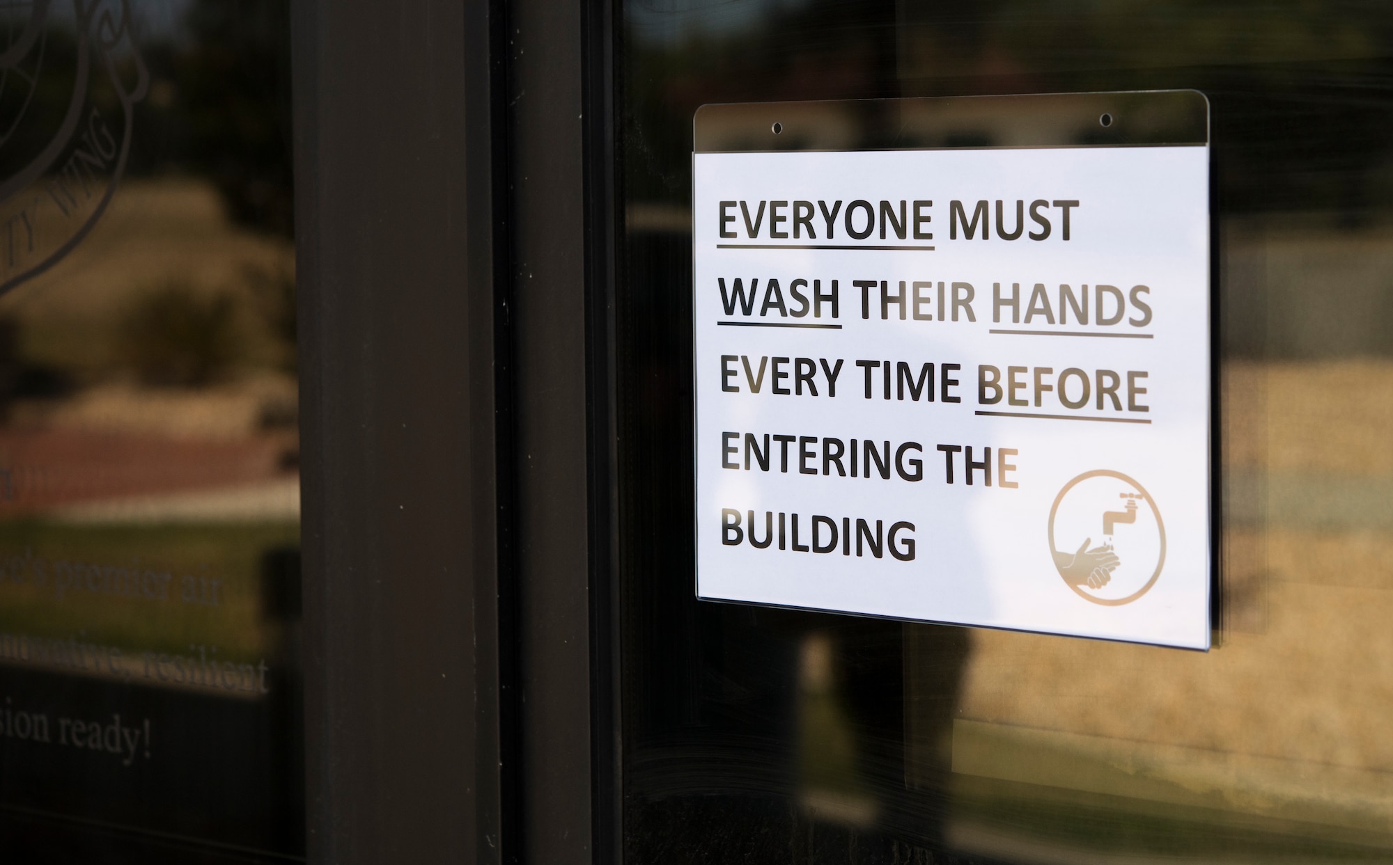 A sign displaying safety messaging in regards to mitigating the spread of COVID-19 hangs outside the headquarters building of the 349th Air Mobility Wing on May 29, 2020, at Travis Air Force Base, California. Travis Air Force Base lowered its health protection class on June 1, opening up the path for members to return to work. (U.S. Air Force photo by 2nd Lt. Daniel Phelps/Released)