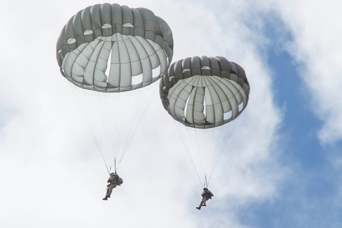 Two airmen descend in the sky wearing parachutes.