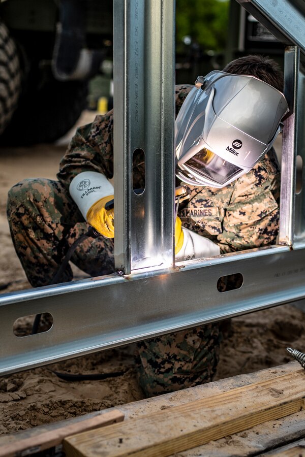 Cpl. Ricardo Torres Vasquez, a metal worker with Special Purpose Marine Air-Ground Task Force - Southern Command, tacks together a roof support during a general exercise at Marine Corps Base Camp Lejeune, North Carolina, April 13, 2020. The beams will be used to create the roof of the building the Marines have constructed. The GENEX includes training events such as engineering projects and evacuation control center training scenarios that will help build the SPMAGTF-SC for their final certification exercise. These training events also provide the Marines and Sailors with real-world scenarios to prepare them for their deployment to assist partner nation militaries in Latin America and the Caribbean. Torres Vasquez is a native of Forest Grove, Oregon. (U.S. Marine Corps photo by Cpl. Benjamin D. Larsen)