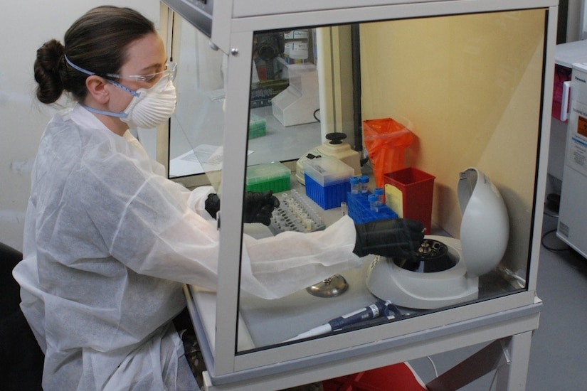 : A woman in protective gear conducts a diagnostic test in a medical laboratory.