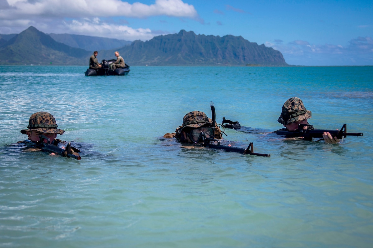Three Marines holding weapons stand with their heads just above water.