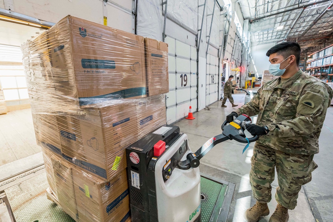 A soldier wearing a mask works with packages stacked in a room.