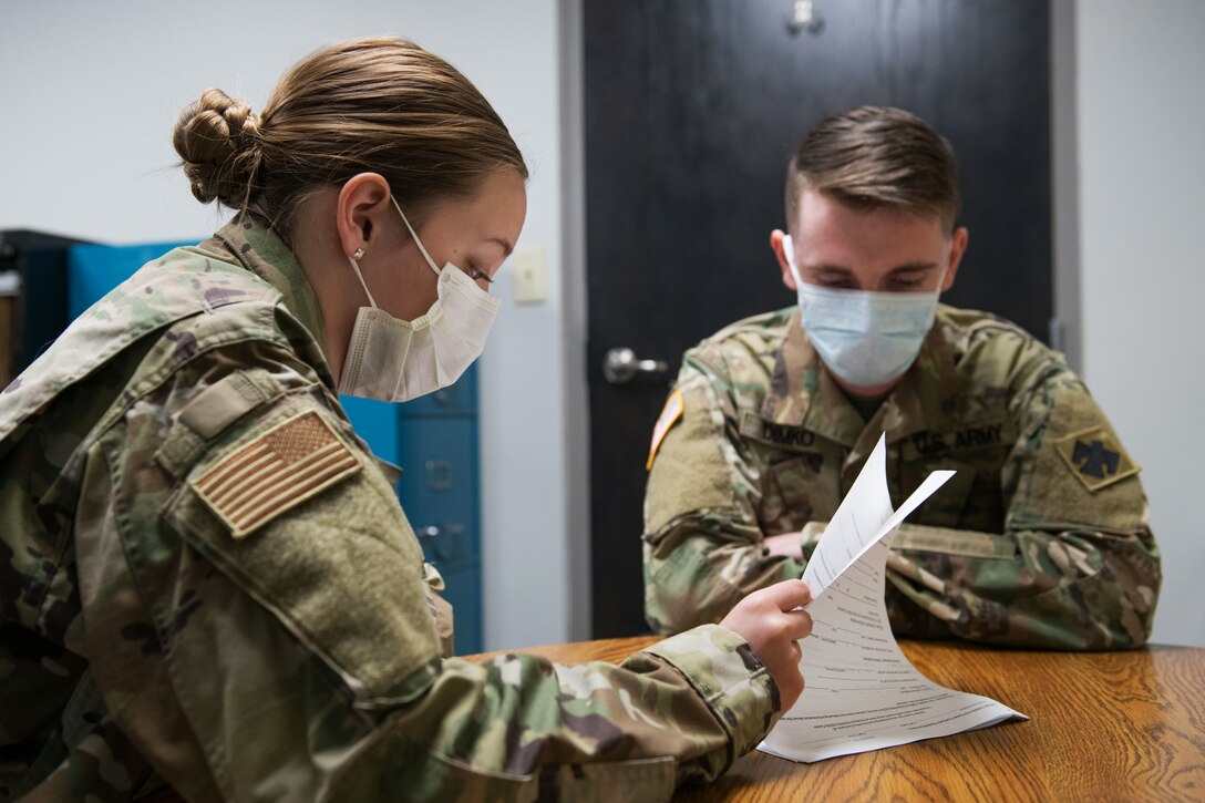 An airman and a soldier, both wearing masks, review documents for COVID-19 contract tracing.