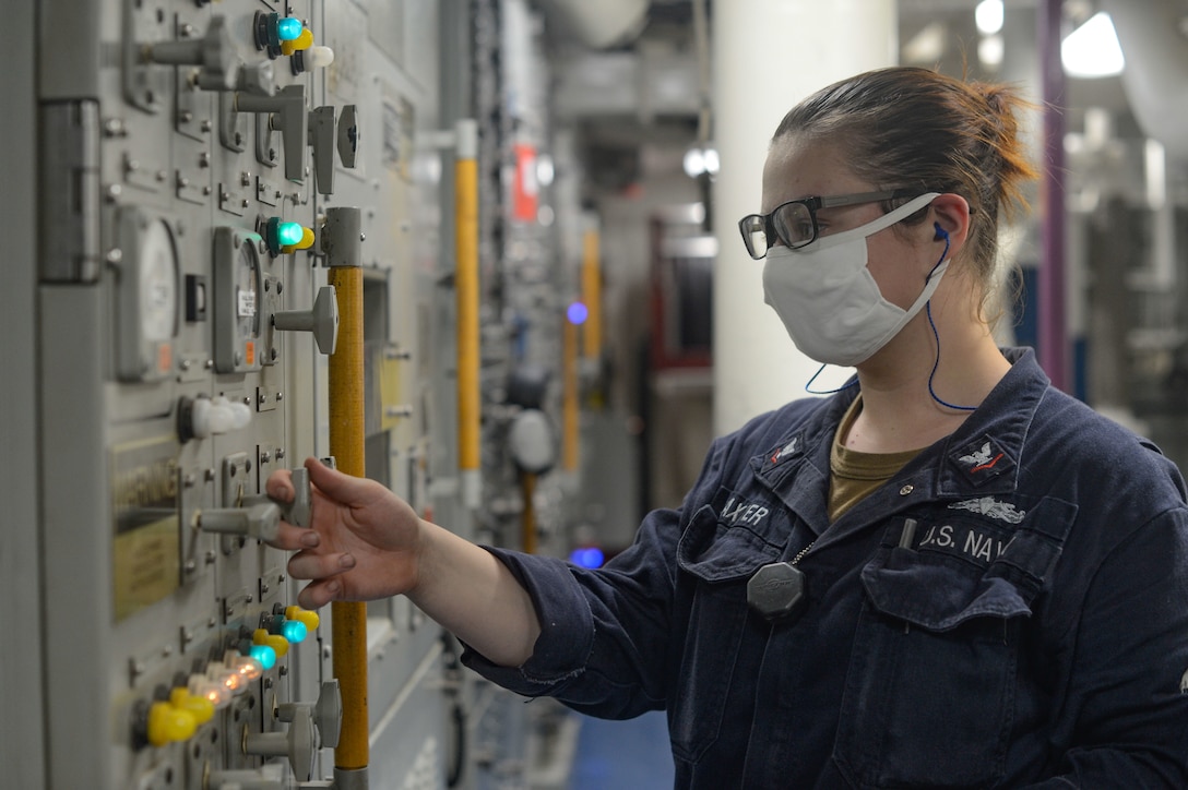 A sailor wearing protective gear touches a switchboard.