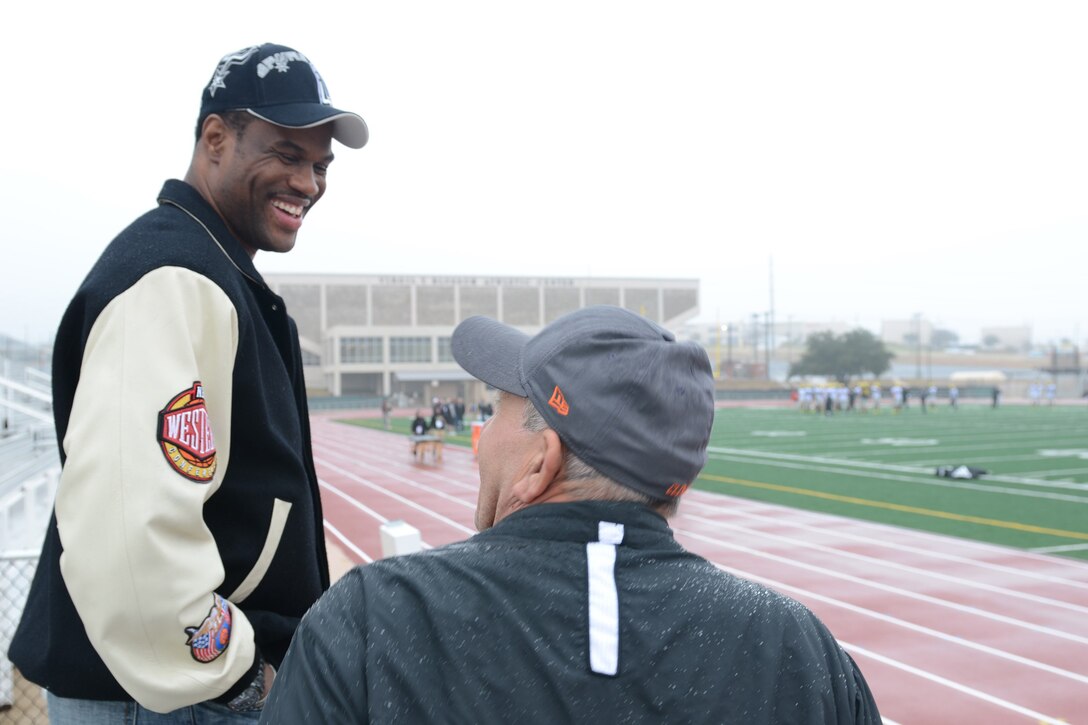 Two men chat beside an athletic field track