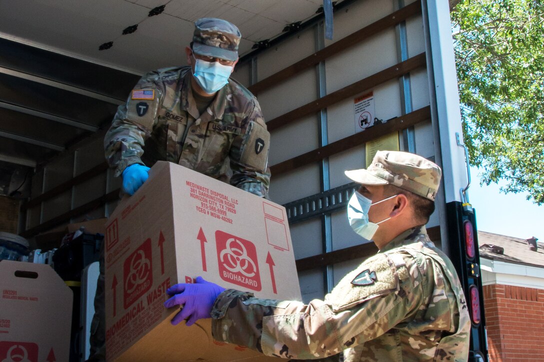 Service members wearing masks and gloves unload a box from a large truck.