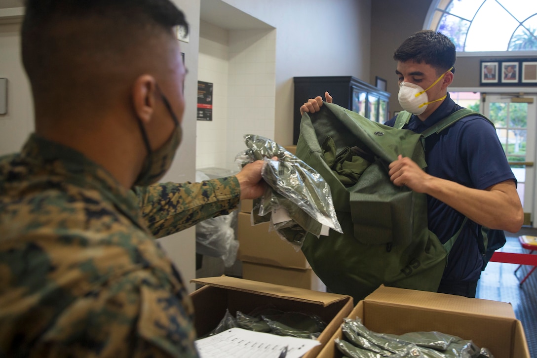 A service member in a mask hands a package to a young man who is also wearing a face mask.