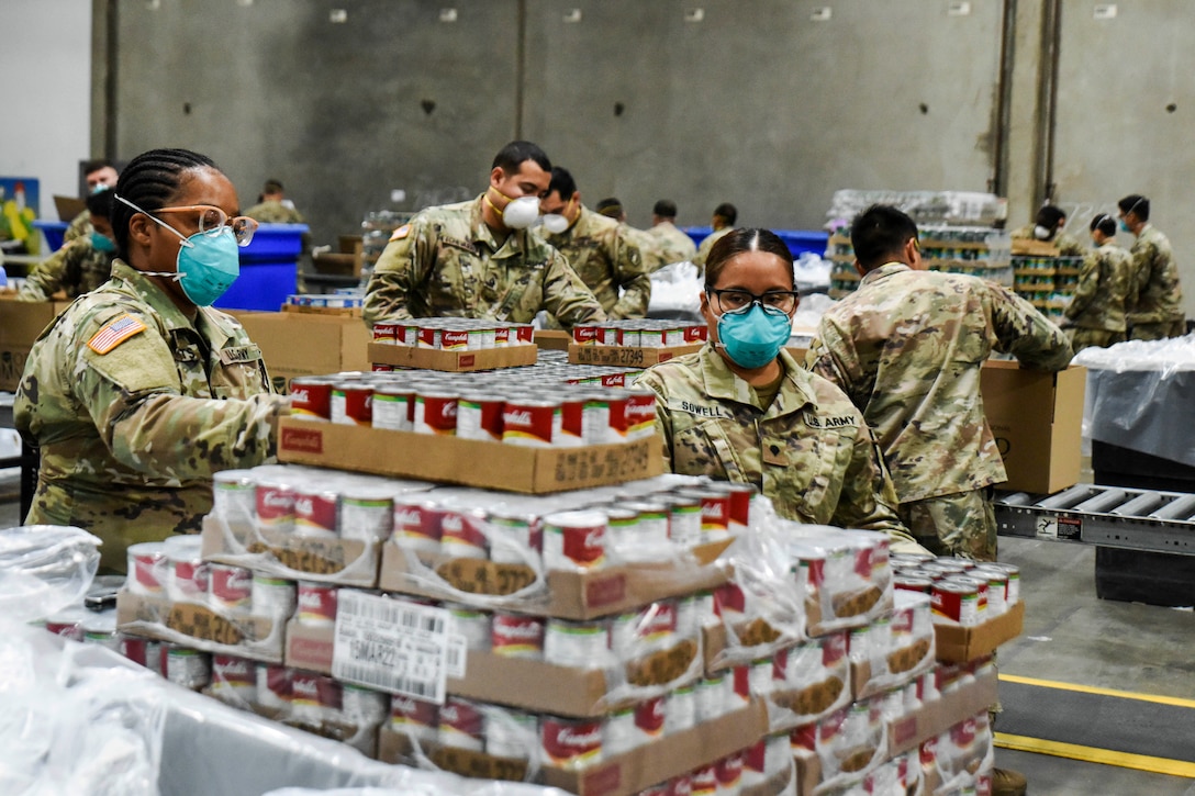 Army National Guardsman in masks help assemble emergency food kits.