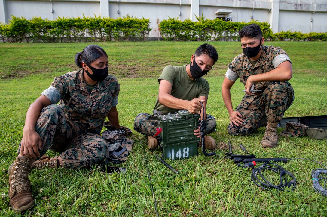 Three Marines sit on grass working on a radio.