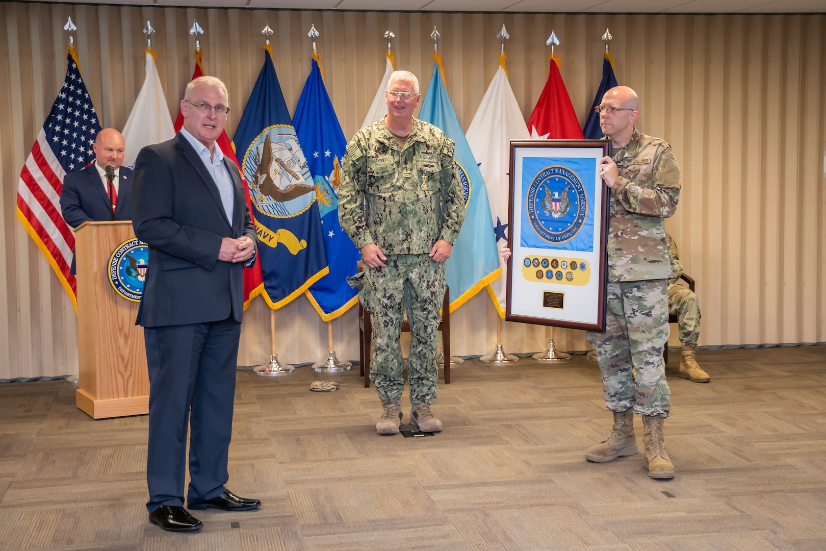 Three men stand, one holding a framed flag