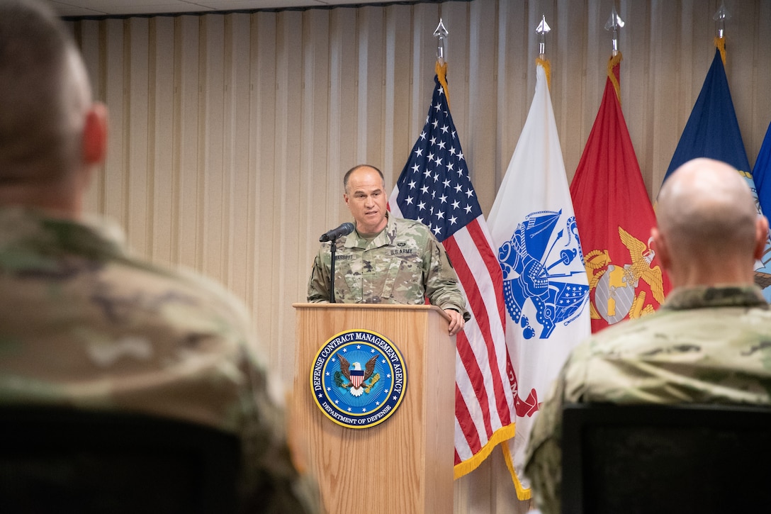 An Army general speaks from a podium in front of flags