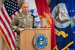 A man in uniform speaks from a podium in front of flags
