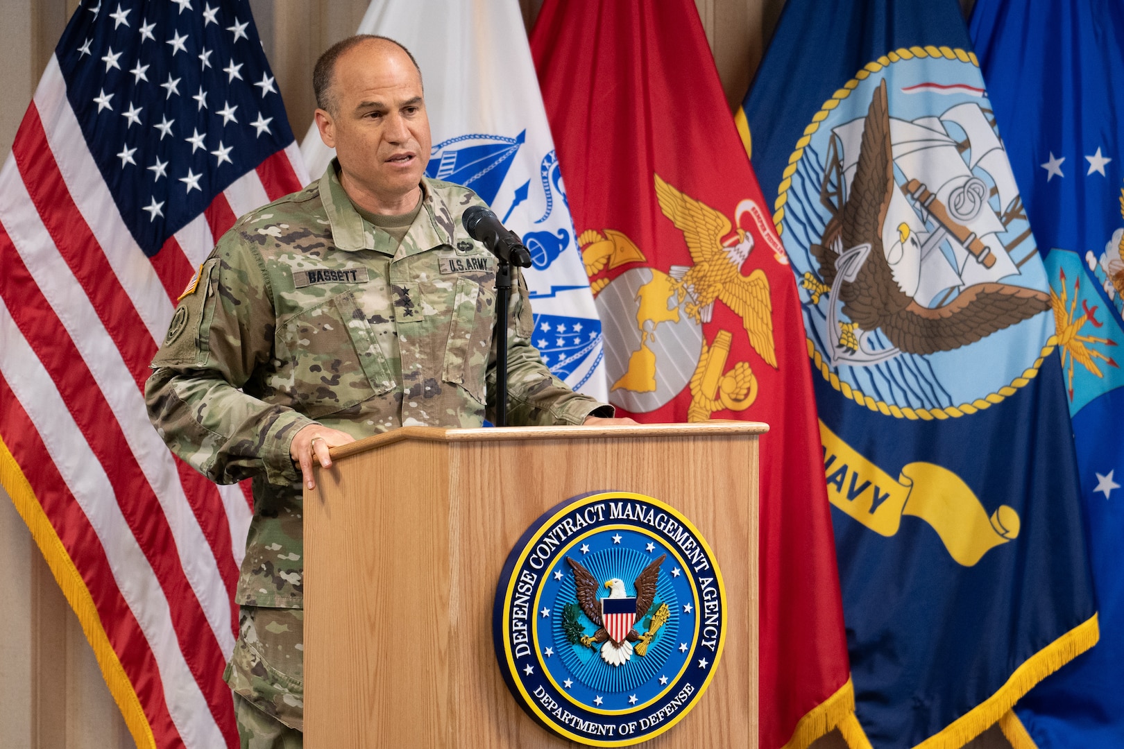 A man in uniform speaks from a podium in front of flags