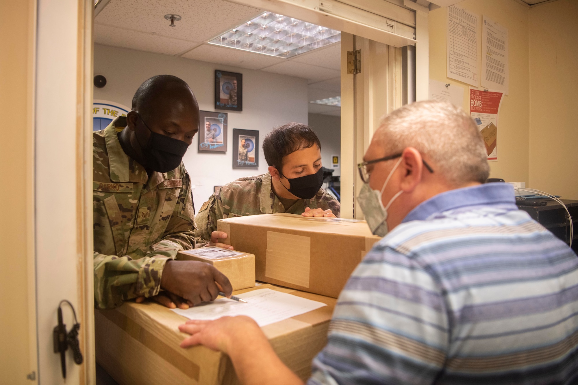 Staff Sgt. Isaac Darko, left, Defense Courier Station Mildenhall defense courier, and Tech. Sgt. Raul Pedroza, right, DCS Mildenhall noncommissioned officer in charge, review asset information with a customer at RAF Mildenhall, England, June 2, 2020. Defense couriers oversee the processing, storage and transportation of sensitive materials. (U.S. Air Force photo by Airman 1st Class Joseph Barron)