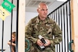 man in green camouflage uniform holds a drill while a young boy sits behind him.