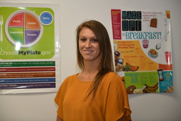 Photo shows a woman standing in front of two nutrition posters.