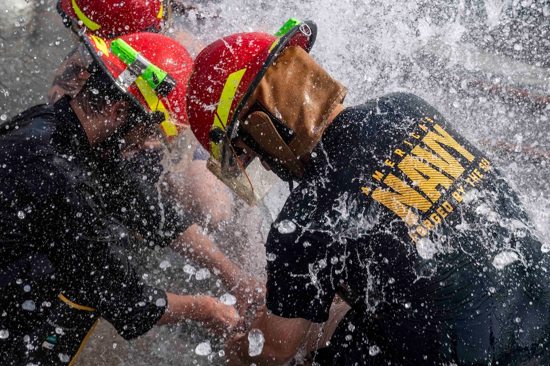 Two sailors work to patch a simulated ruptured pipe as water comes rushing out.