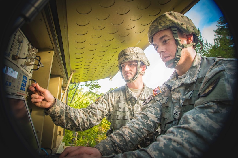 Two soldiers work with communications equipment.