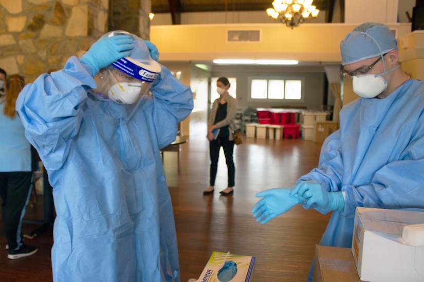 Two service members put on blue personal protective equipment.