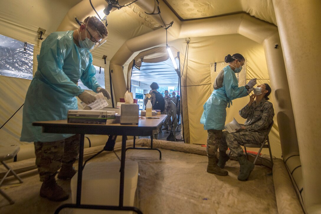 Soldiers in protective medical gear work inside a tent-like structure.