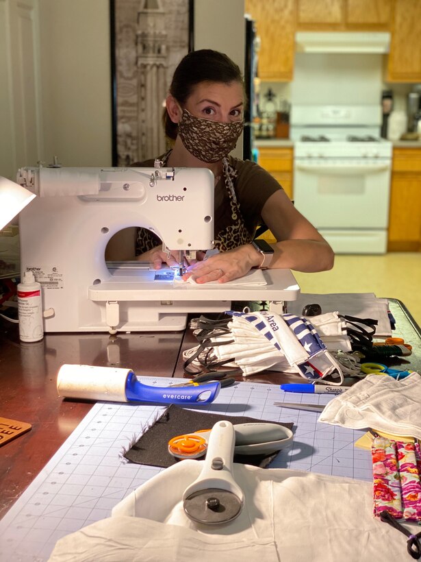 A woman sews masks at her sewing machine while wearing a mask.