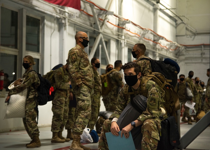 Airmen wear masks and carry bags in a terminal.