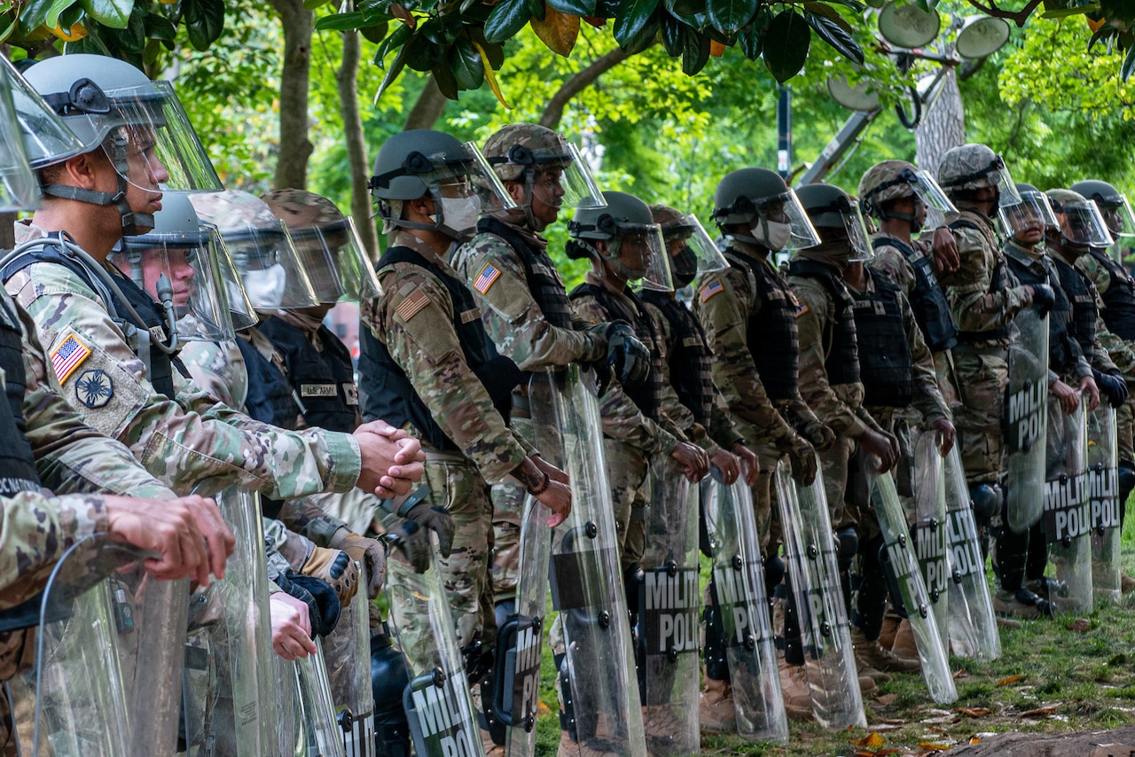 Guardsmen with shields in front of them stand in formation.