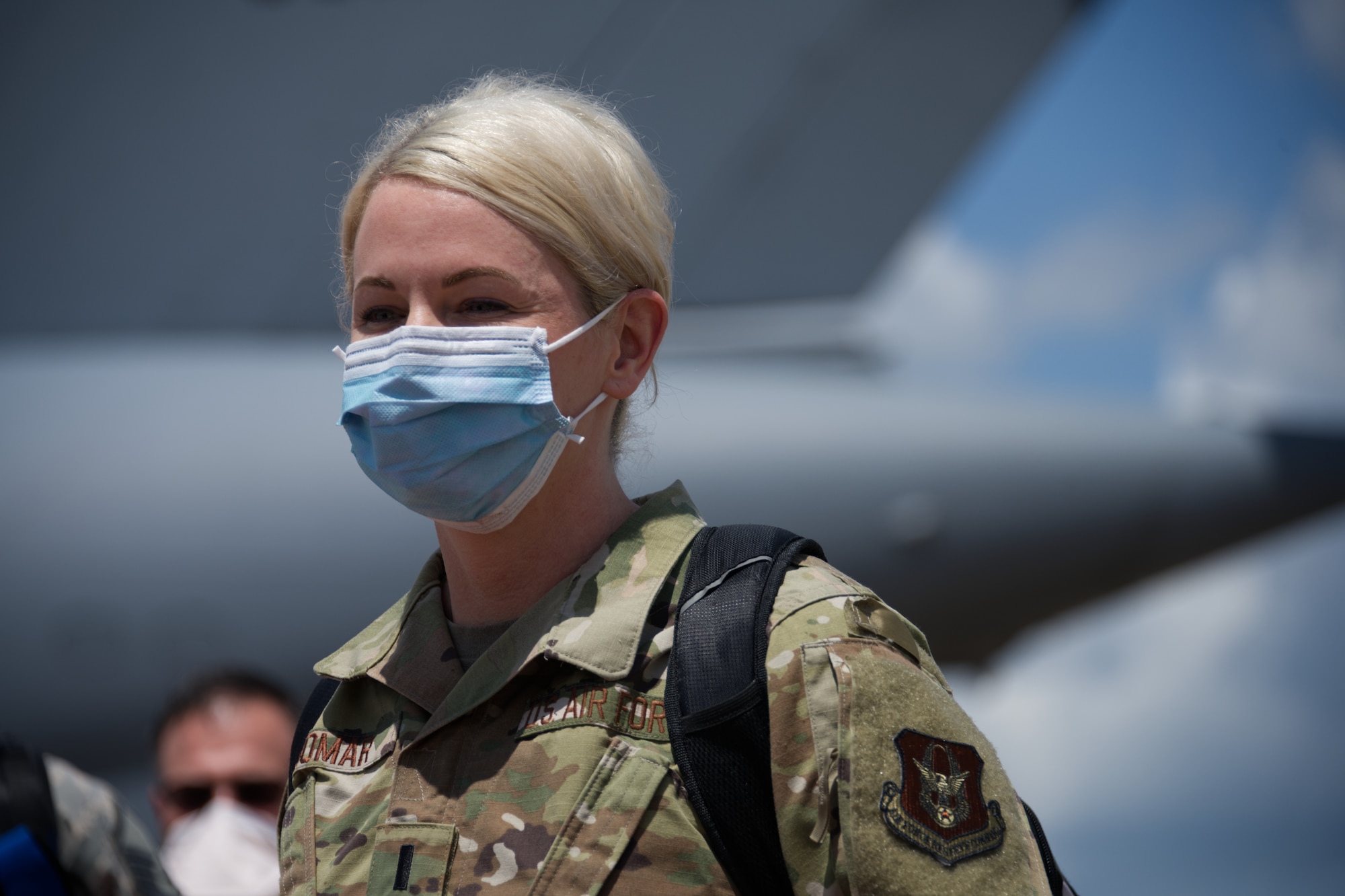 Airman stares across flight line while wearing mask.