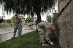 Spc. Jamie Harrison and Sgt. Aaron Crane of Kosovo Force Regional Command East Liaison Monitoring Team “Kilo 20” pick up trash along a creek of Vitina/Viti, Kosovo, June 5, 2020. LMT personnel from “Kilo 20” out of Camp Bondsteel and Maneuver Battalion personnel out of Camp Nothing Hill participated in area beautification in observation of World Environment Day.