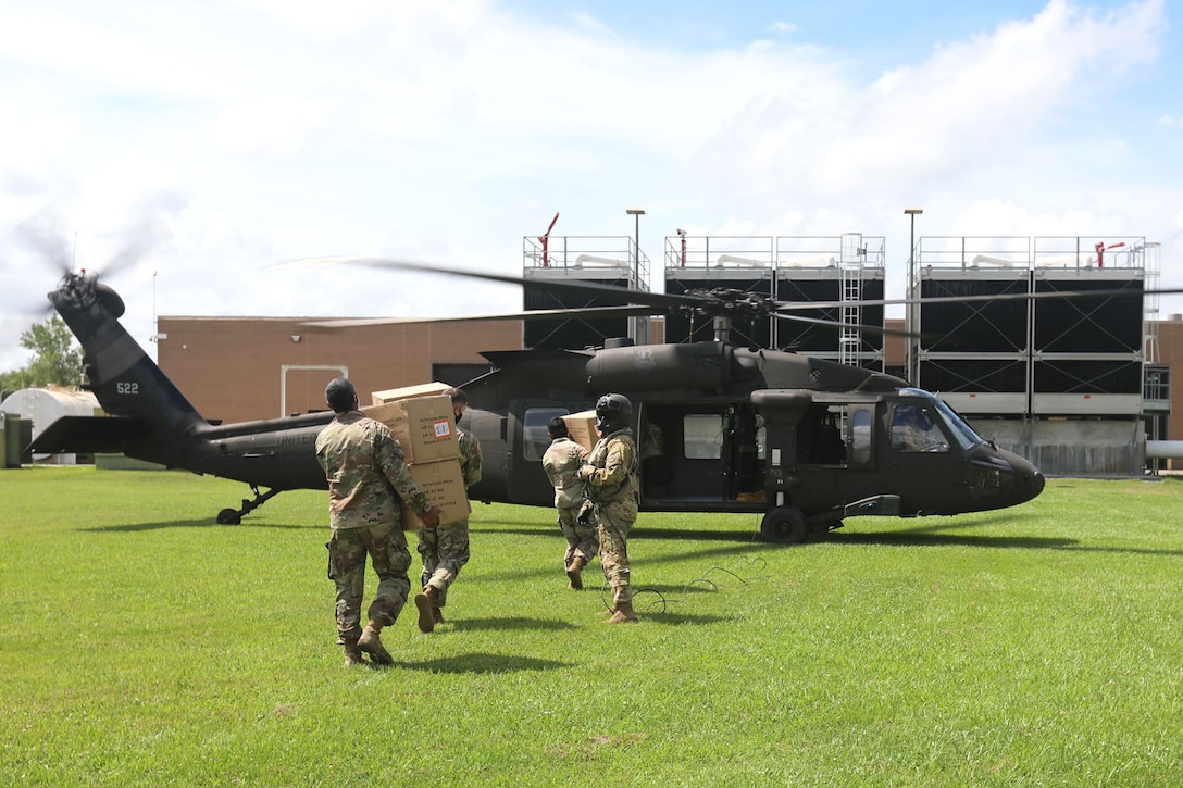 Soldiers carry boxes of supplies to a military helicopter.